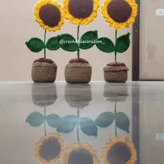 A trio of our crochet sunflower pots, perfect as a set for decorating a windowsill or table. Their reflections on the glass table highlight their clean, symmetrical design.