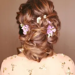 A detailed shot of this stunning party hairstyle. This intricate, messy bun is woven with delicate purple and white flowers, making it perfect for a sangeet or reception guest.