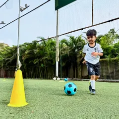 A U6 player focuses intently as he dribbles past a cone, learning the basics of ball movement on our professional turf.