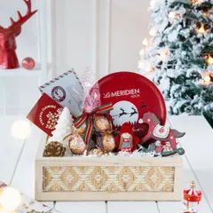 The 'Winter Wonderland' hamper fully assembled in a woven wooden box, set against a snowy Christmas tree backdrop for a magical, festive feel.