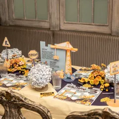 The construction-themed tablescape for Raghav's 3rd birthday, featuring personalized placemats, "Work Area" signs, and floral arrangements in yellow and blue.