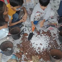 Children work together, using small shovels to mix the crushed eggshells into the soil. This collaborative activity teaches them about teamwork and caring for the earth.