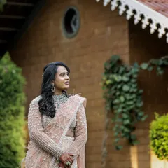 A candid and elegant portrait of a bride at her reception, looking off to the side in a beautifully embroidered lehenga, captured in a lovely garden setting.