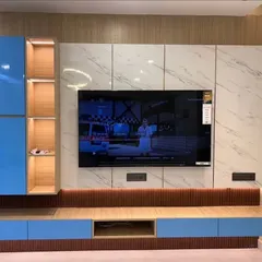 A bold and modern TV unit design featuring vibrant blue high-gloss cabinets against a white marble-finish wall. The unit includes open, backlit wooden shelves for display and a floating console that keeps the look clean and contemporary.