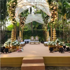 This unique mandap design for an outdoor wedding features a modern arched roof structure draped in sheer fabric and adorned with clusters of white flowers, creating an airy and elegant space.