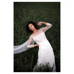 An editorial bridal portrait in a field of tall grass. The pose, the flowing veil, and the soft, natural light give this image a high-fashion, romantic feel.