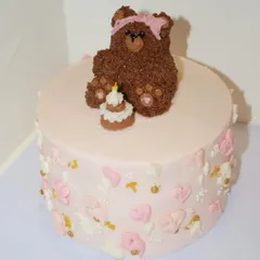 An adorable teddy bear themed birthday cake. This one features a cute, fuzzy buttercream bear wearing a pink bow, sitting next to its own tiny birthday cake.
