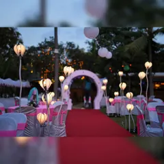 A beautiful red carpet entrance for an outdoor party, lined with unique floral-shaped standing lamps that illuminate the pathway.