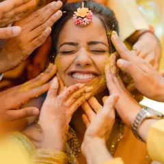 A bride's smile, framed by the loving hands of her family. This is the heart of the Haldi ceremony, a ritual of blessings and happiness.