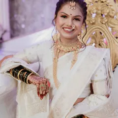 A beautiful bride in a classic white saree, her smile lighting up the frame. This portrait highlights her traditional gold jewelry and the intricate henna on her hands.
