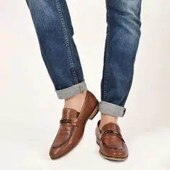 A lifestyle shot showing brown leather loafers paired with rolled-up denim, creating a stylish and relatable context for the product.