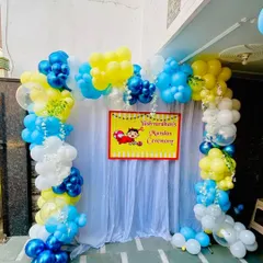 A simple and bright backdrop for "Yashvardhan's Mundan Ceremony." This outdoor setup includes a white curtain, a custom banner, and a colorful balloon arch in yellow, blue, and white.