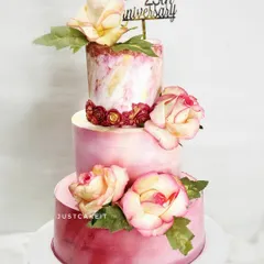 An elegant three-tier cake for a 25th wedding anniversary. The design features a soft pink marble effect, delicate sugar flowers, and a touch of gold.