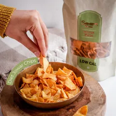 A hand reaches for a Diet Jowar Chip from a brass bowl. These low-calorie, baked chips are a wholesome and delicious choice for better snacking.