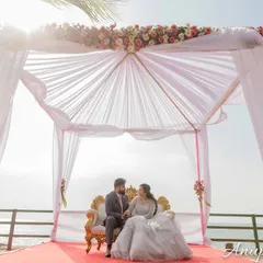 A wide-angle shot of a couple seated under a beautiful canopy by the sea. This photo establishes a sense of place and the grand, romantic setting of their shoot.