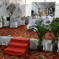 For this corporate setup, I created a raised platform area with a printed backdrop showing the client's project. The space includes carpeted flooring, skirted round tables, and potted plants to complete the look.