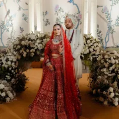 A portrait of modern royalty. I styled Navya and Avi against a hand-painted backdrop with soft floral arches, coordinating her vibrant red Falguni Shane Peacock lehenga with his elegant ivory sherwani for a harmonious and regal look.