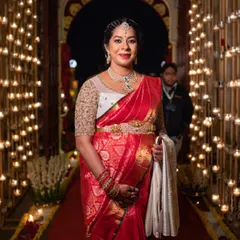 An expectant mother looking radiant at a wedding in a red Banarasi saree. Her custom white blouse with sheer embroidered sleeves provides an elegant and comfortable fit.