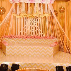 Here is the full view of the beautiful Haldi ceremony stage I designed. The setup features a canopy of hanging floral strings, a tiered seating area with a chevron pattern, and a large brass uruli in the front for the rituals.