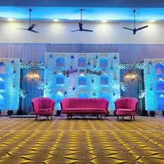 We transformed this hall with a beautiful wedding stage featuring white floral panels and soft blue backlighting. The design includes traditional arch-shaped niches and vibrant pink seating, creating a perfect blend of classic and contemporary styles.
