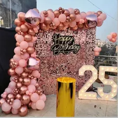 A chic outdoor 25th birthday setup on a rooftop. The rose gold sequin wall is framed by a matching balloon arch, with a large light-up number '25' making a bold statement.