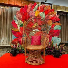 A vibrant and fun photobooth designed for a Mehendi ceremony. The peacock chair is set against a backdrop of colorful, fan-shaped leaves, creating a bold and festive look.