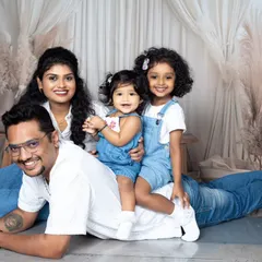A playful family portrait with two daughters sitting on their father's back as he lies on the floor.