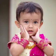 This close-up just melts my heart. She is wearing a simple yet elegant cream and pink silk pavadai, a traditional outfit that is perfect for a baby's first festival or ceremony.