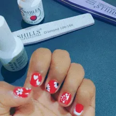 A vibrant red gel polish on short, natural nails. Each nail features unique, hand-painted art, including tiny hearts and delicate white flowers, showing how much fun you can have with any nail length.