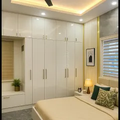 A different angle of the contemporary bedroom, showcasing the floor-to-ceiling wardrobe in a sleek, high-gloss white finish. The design includes a built-in seating nook by the window, maximizing both storage and functionality.