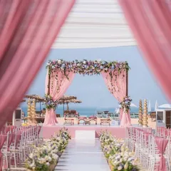 A dreamy beachside wedding ceremony, with a beautiful floral mandap and pink-draped aisle looking out over the ocean.