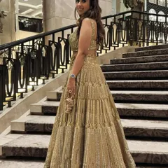 A full-length shot of a client ready for a grand event. Her hair is styled in soft waves, and the bold smokey eye makeup complements her glamorous gold lehenga perfectly.