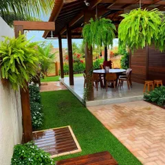 We design outdoor living areas that feel like a natural extension of your home. Here, a covered patio is enhanced by lush hanging ferns and a perfectly manicured lawn, creating a private escape for relaxation and entertainment.
