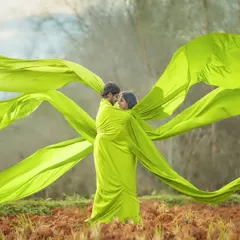 Wrapped in love and vibrant colour. This creative pre-wedding shot uses a flowing green fabric to create a sense of movement and intimacy, set against a simple, natural backdrop.