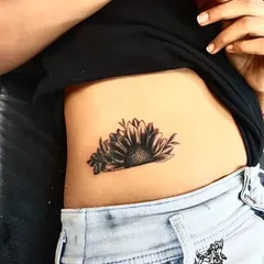 After: A black and grey sunflower design was used to cover the old tattoo. The placement and shading of the flower completely hide the name, transforming the area with a popular and positive floral design.