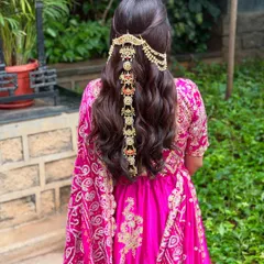 An elegant half-updo for a Mehendi ceremony. The hair is styled in soft waves and accessorized with a stunning, intricate golden hairpiece that drapes down the length of the hair.