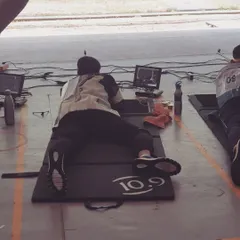 A shooter practices in the prone position, a fundamental aspect of certain rifle events. We coach athletes on body stability and rifle support to maximize accuracy from this position.