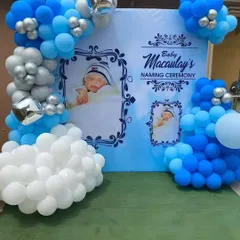 A personalized naming ceremony backdrop in blue and white. The design features photos of the baby, creating a heartfelt and custom touch, framed by a balloon arrangement.