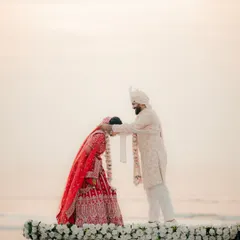 A moment of reverence and blessing during a beach wedding. The groom places sindoor on the bride's forehead with the serene ocean behind them.