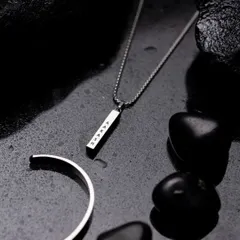 A styled flat lay of a men's silver necklace and bracelet set. The dark, wet slate and stones create a moody and sophisticated atmosphere that elevates the product.