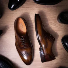 An overhead shot of classic brown and black formal shoes. The composition creates a sense of variety and choice, while the clean lighting on the wood-textured floor adds a touch of class.