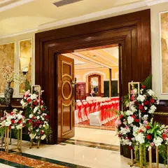A peek into a grand ballroom celebration, with the entrance framed by beautiful red and white floral arrangements on golden stands.