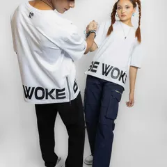 A studio shot for a streetwear brand, focusing on the back and side details of the graphic tees. The pose highlights the zipper detail and bold "WOKE" text.