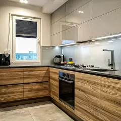 A beautiful two-tone kitchen design combining warm, wood-grain lower cabinets with sleek, high-gloss upper cabinets. The under-cabinet lighting provides excellent task illumination on the dark countertop.