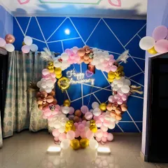 A full circular balloon arrangement in pink, white, and gold for an anniversary celebration at home, complete with a neon sign and feather accents.