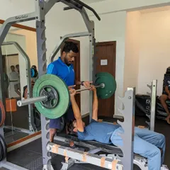Assessment week is crucial for program design. Here, an athlete performs a bench press under the watchful eye of a strength coach to establish baseline strength levels.