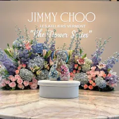 A product display designed for the launch of Jimmy Choo's 'The Flower Series'. The new handbag is presented on a pedestal, framed by an exquisite arrangement of pastel hydrangeas, roses, and lilies, perfectly reflecting the collection's floral elegance.