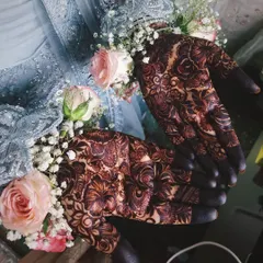 A stunning bridal portrait showcasing the dark, elegant stain of the mehendi, perfectly complemented by floral bracelets and a beautiful gown.