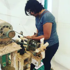 With intense focus, a participant learns to handle the chisel on the spinning lathe. This is the most crucial step in toy making, where the raw wood begins to take on a new form under the creator's touch.