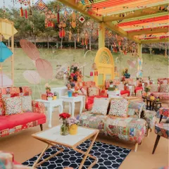 A vibrant and eclectic lounge for a Kite Carnival event, featuring patchwork sofas, colorful overhead drapes, and hanging traditional crafts that create a festive and bohemian atmosphere.